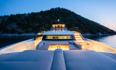Danlou: Foredeck sunpads and lounge seating at dusk with lit superstructure and wooded hill behind