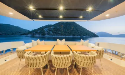 Danlou: Aft deck dining table with woven chairs and cushioned bench facing a calm bay and island at dusk