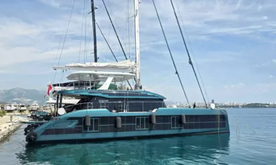 Midori Eco: Catamarã a vela azul esverdeado atracado de popa em uma marina com montanhas ao fundo