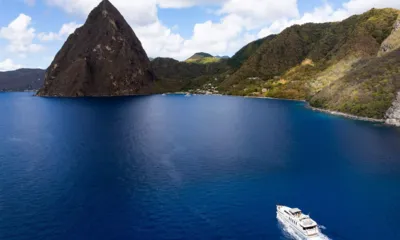 Lady Gerts: Iate navegando sobre águas azul profundo sob um pico alto e pontiagudo e litoral verde