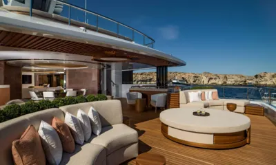 Life Saga: Lounge externo no convés com sofás curvos, pufe redondo e área de jantar ao lado de penhascos rochosos
