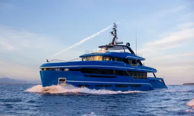 Sui Generis: Yate azul navegando levantando una ola de proa con luz de atardecer