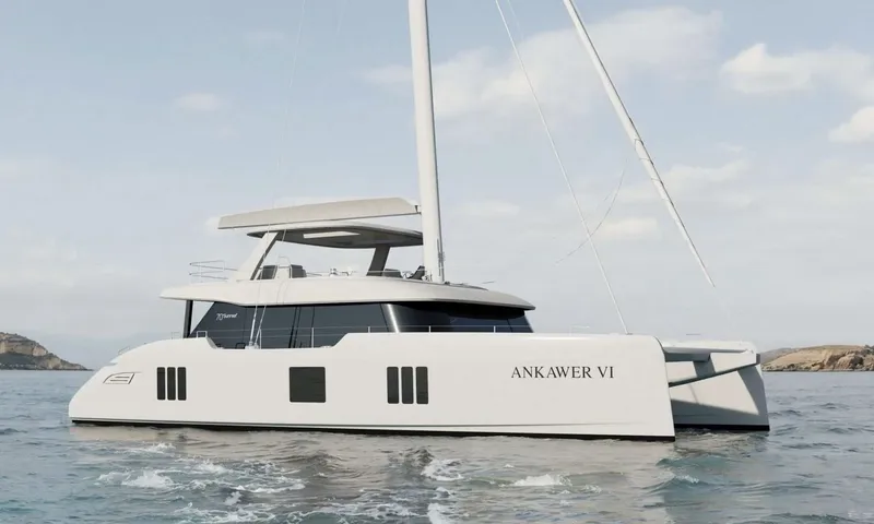 Ankawer VI: White sailing catamaran with tall mast and flybridge hardtop cruising on calm sea near rocky shores