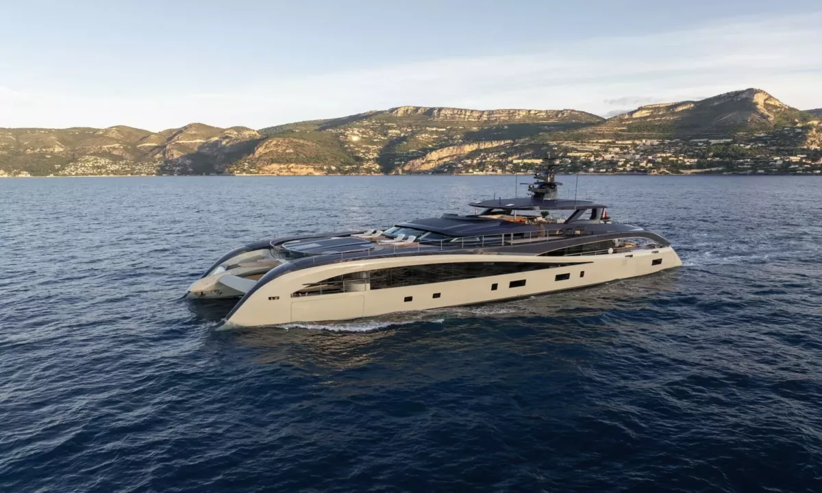 Seawolf X: Beige and dark grey yacht cruising on blue sea with hills and a coastal town behind