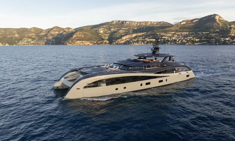 Seawolf X: Beige and dark grey yacht cruising on blue sea with hills and a coastal town behind