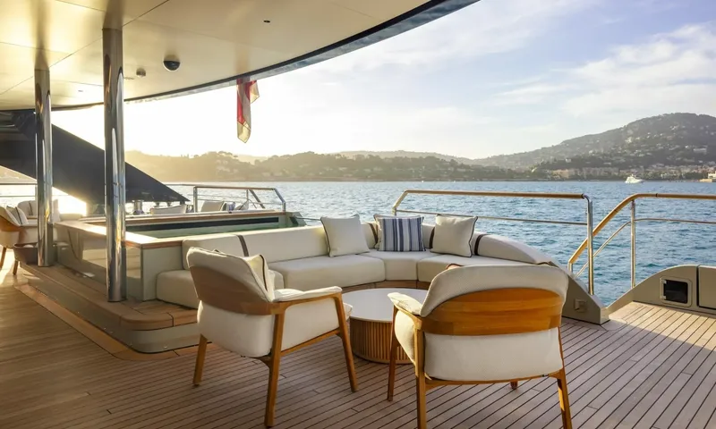 Seawolf X: Aft deck lounge with white sofa, armchairs and coffee table beside a pool, overlooking a hilly coast