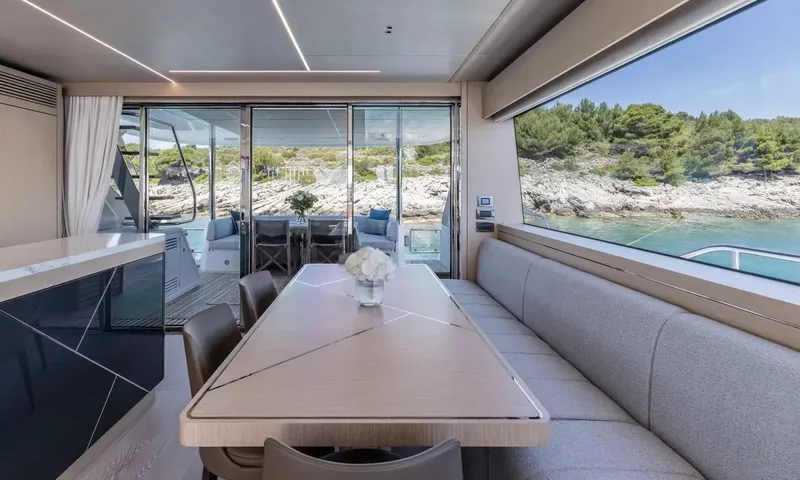 Ascend: Wooden dining table with flowers, bench seating and glass doors open to the aft deck
