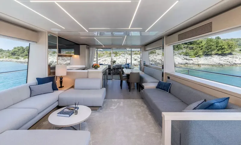 Ascend: Bright saloon with grey sofas, coffee table and dining area leading to the aft deck