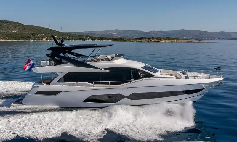 Ascend: Motor yacht cruising at speed across blue water with hills behind