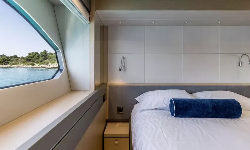 Ascend: Close view of a bed with navy bolster beside an angled window over the water