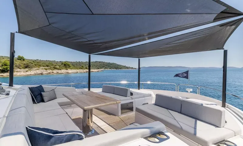 Ascend: Shaded foredeck lounge with wraparound seating and wooden table overlooking calm sea and coast