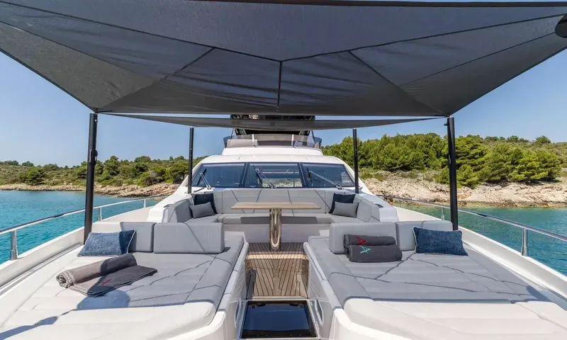 Ascend: Foredeck sunpads and lounge seating under a dark shade canopy near a rocky wooded shore