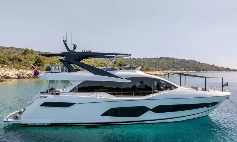 Ascend: White motor yacht with dark hardtop anchored in turquoise water near a wooded rocky shore