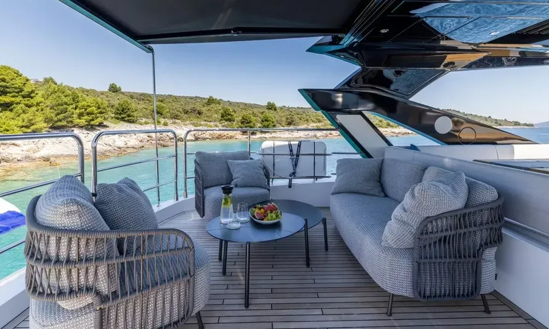 Ascend: Upper deck lounge with woven armchairs, sofa and coffee table with fruit bowl by the shore