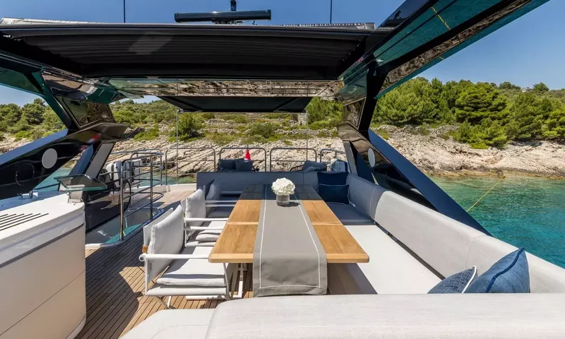 Ascend: Upper deck dining table with bench seating and chairs under a hardtop near a rocky shore