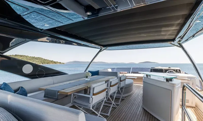Ascend: Shaded upper deck dining area with long table, chairs and bar counter overlooking the sea