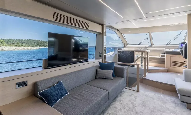 Ascend: Bright saloon with grey sofa, television and large windows, steps leading to the helm