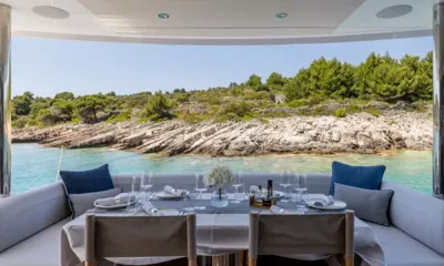 Ascend: Aft deck table set for a meal with glasses and flowers facing a rocky wooded shore