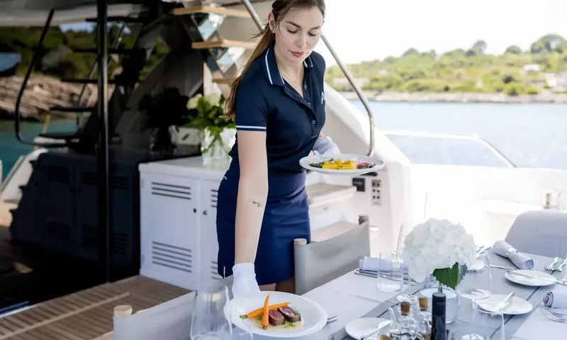 Ascend: Crew member in uniform serving plated food at a set outdoor dining table