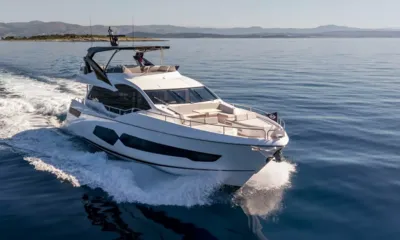 Ascend: White motor yacht cruising at speed across calm blue water with hills behind