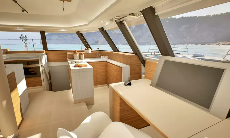 Elly II: Interior helm desk with chair facing large windows, kitchen behind