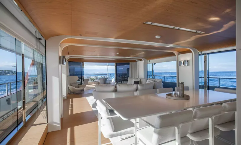 Angel: White dining table with upholstered chairs in front of an open plan lounge with sea views