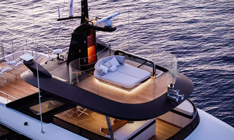 Angel: Top deck daybed with glowing lights behind glass screens beside the mast at dusk