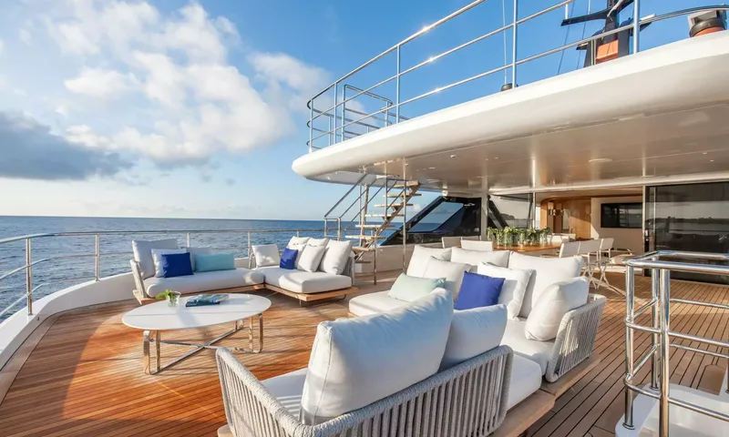 Angel: Teak upper deck lounge with white sofas, blue cushions and stairs to the deck above