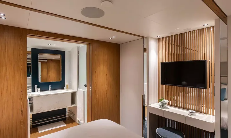 Angel: Cabin corner with wall television on slatted wood and open door to an ensuite basin