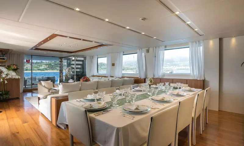 Kristo: Indoor dining table set for ten beside the lounge, with windows overlooking the water
