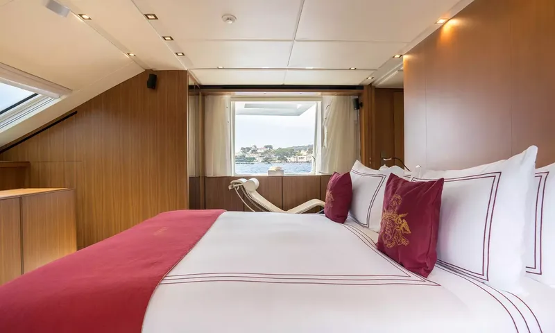 Kristo: Double bed with red cushions facing a window with sea view and lounge chair