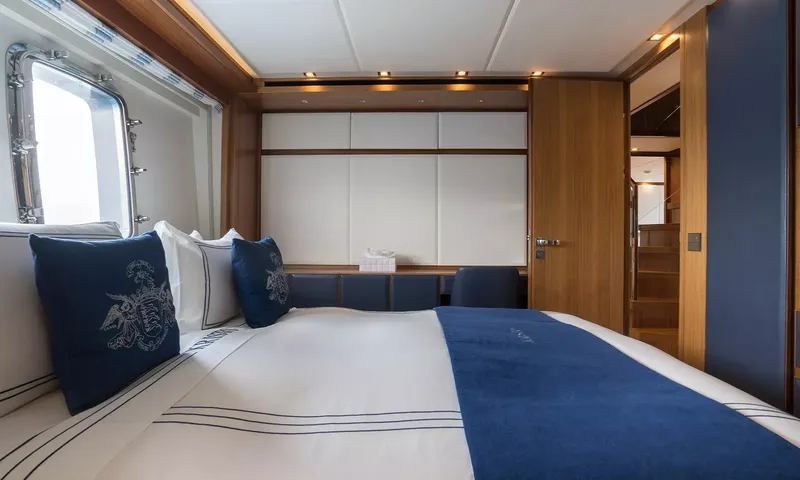Kristo: Double bed with navy cushions beside a porthole, wardrobes and wooden door