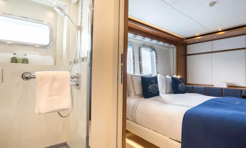 Kristo: Shower with towel in foreground and view through to a double cabin with navy bedding
