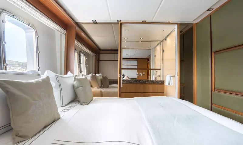 Kristo: View across a double bed with grey cushions toward portholes and the ensuite