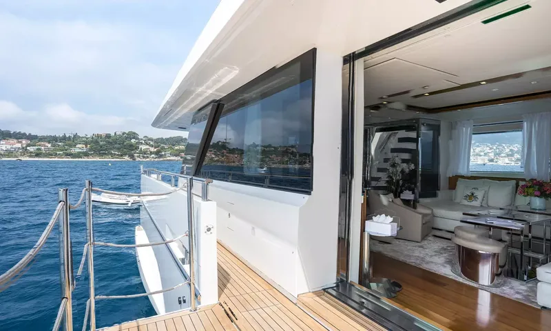 Kristo: Teak side deck beside open glass doors leading into a bright lounge, sea and coastline beyond