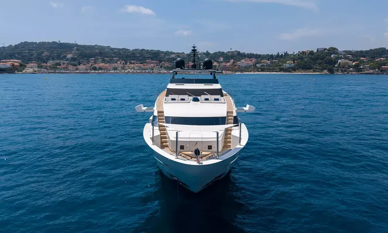 Kristo: Bow view of the white yacht at anchor in front of a hillside coastal town