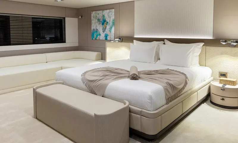 Oriy: Cabine com cama grande branca, manta dobrada, banco aos pés e sofá de canto