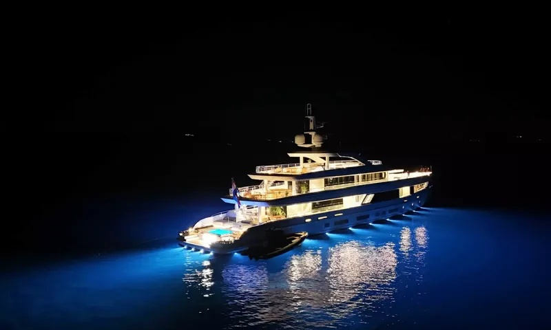Oriy: Iate à noite visto de cima, conveses iluminados e luzes azuis brilhando no mar em volta do casco