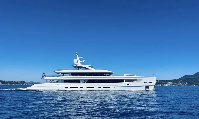 Oriy: Iate branco navegando em um mar azul profundo sob céu limpo, visto de lado, com colinas verdes ao fundo