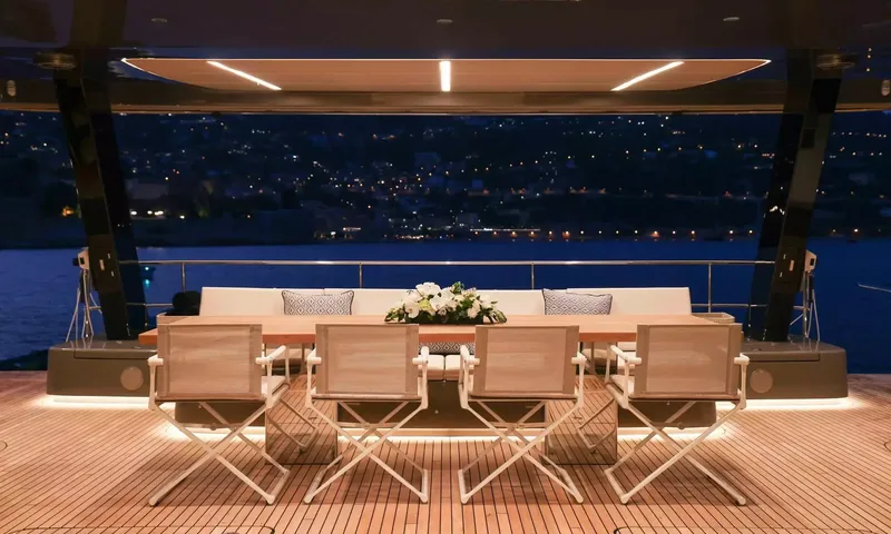 Amitatu: Outdoor dining table with white chairs on a lit teak deck at night