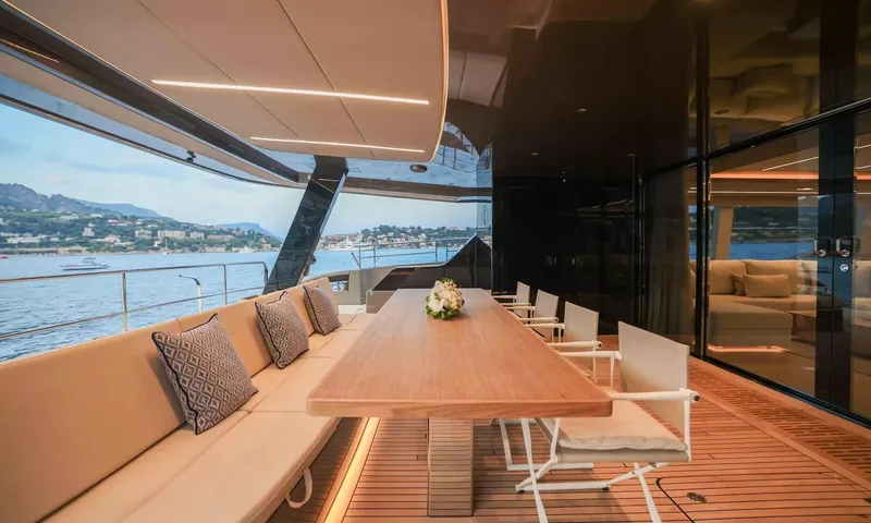 Amitatu: Covered aft deck dining table with bench seating and white chairs beside the saloon doors