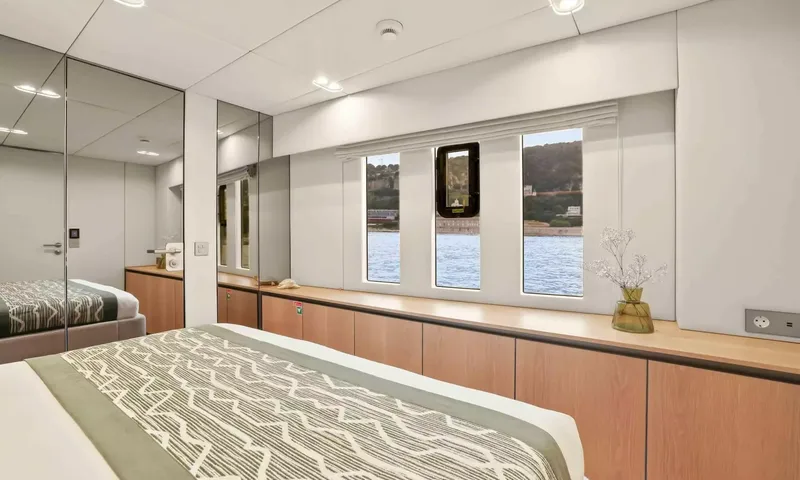 Amitatu: Cabin with bed foot, mirrored wardrobe and windows looking onto the water