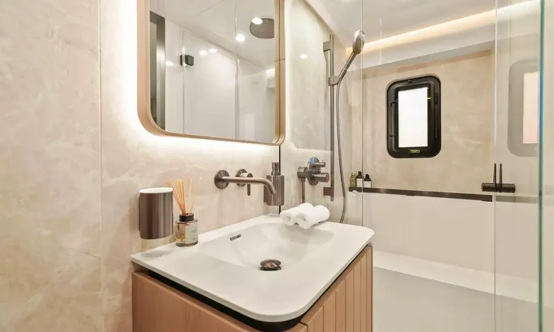 Amitatu: Bathroom sink with backlit mirror, rolled towels and glass shower with porthole