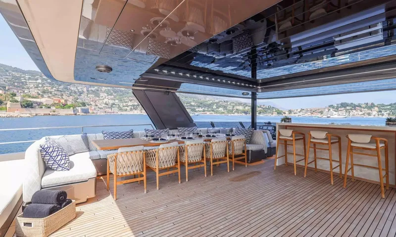 Amitatu: Shaded deck with set dining table, cushioned sofa and bar stools overlooking a hillside harbour