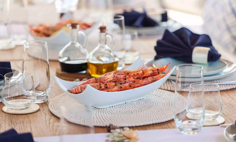 Amitatu: White dish of cooked prawns on a set table with glasses and oil bottles