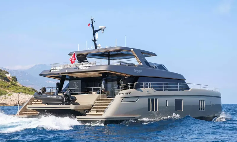Amitatu: Grey power catamaran cruising on blue sea with a tender stowed at the stern