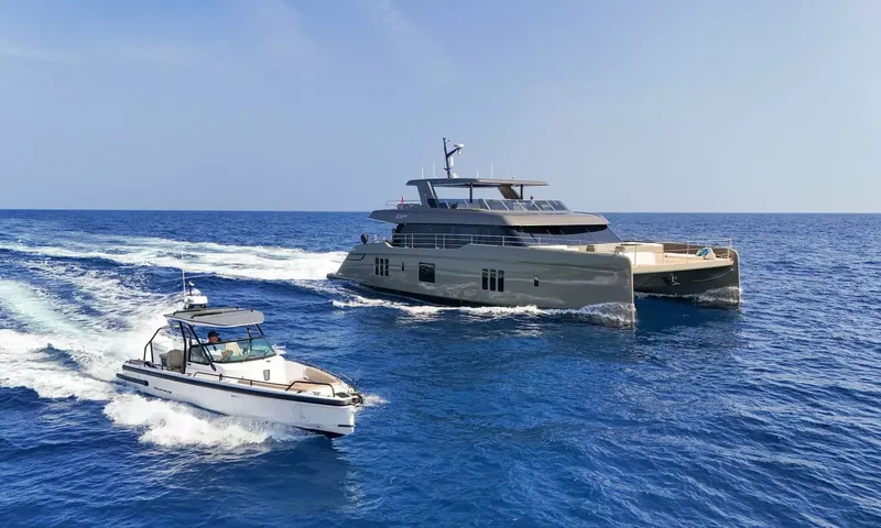 Amitatu: Catamaran under way on open blue sea followed by a white tender