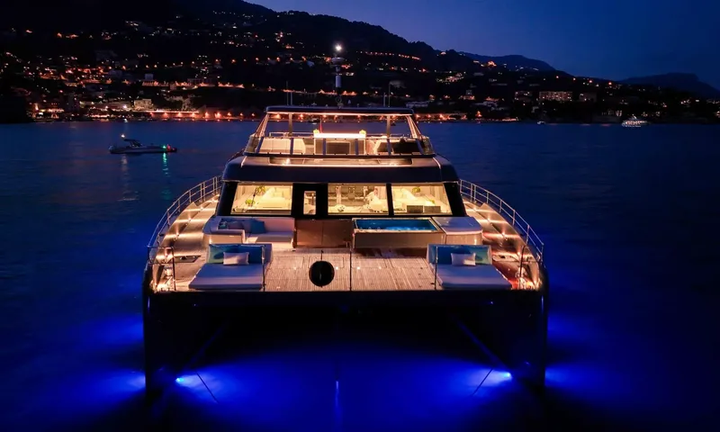 Amitatu: Catamaran bow at night with lit foredeck jacuzzi, sunpads and blue underwater lights