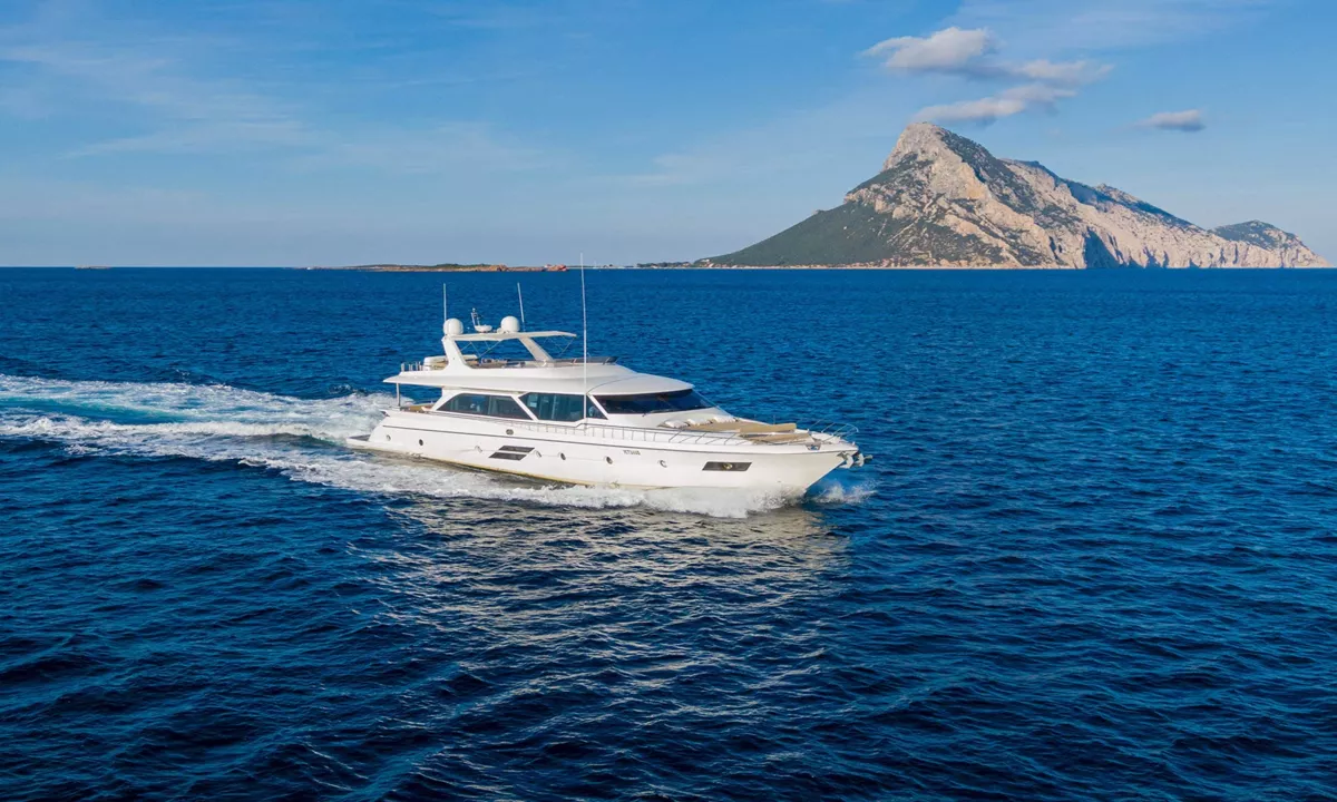 Enjoy I: Iate a motor branco navegando em mar azul profundo com uma ilha rochosa ao fundo