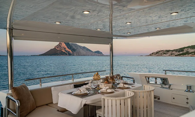 Enjoy I: Mesa posta para o jantar no convés de popa ao entardecer, com uma ilha rochosa do outro lado do mar
